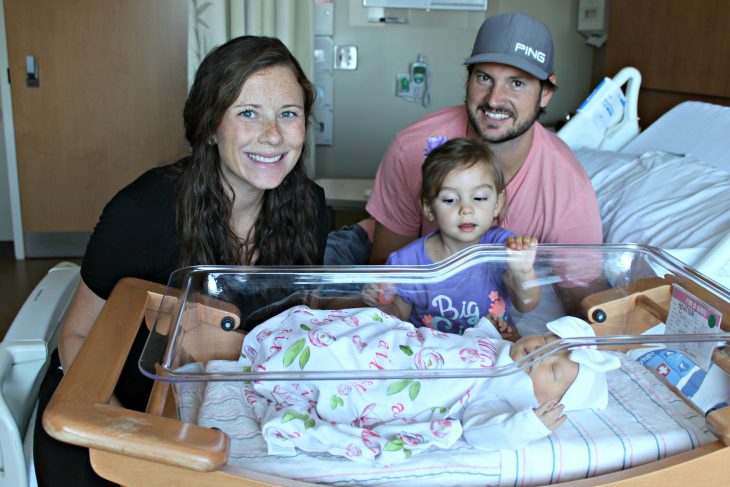 Mom, Dad, and Daughter peeking at a newborn baby
