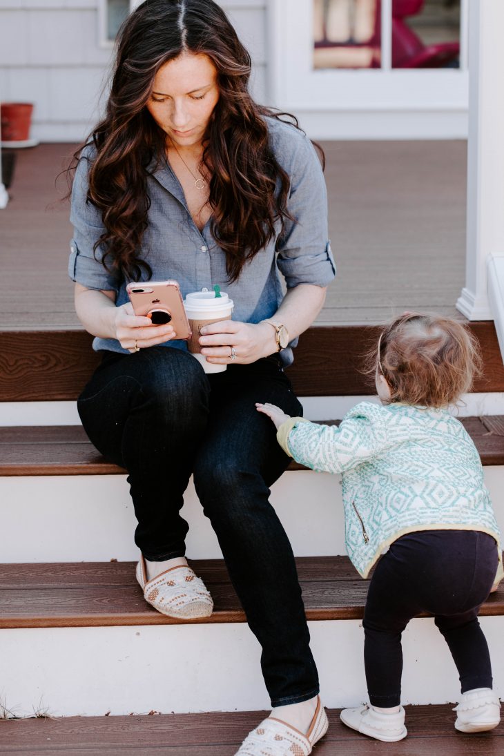 Woman holding coffee and cell phone and child 