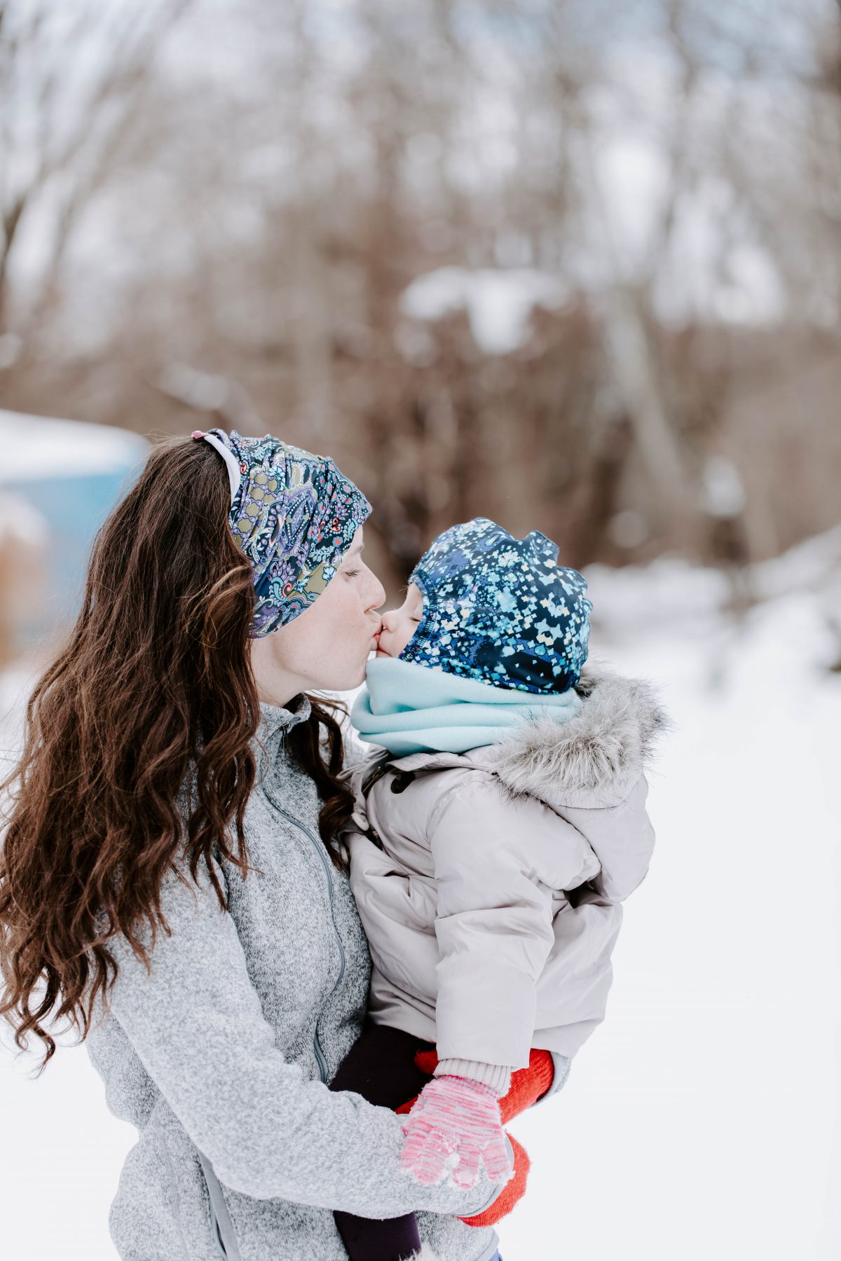 Mom wearing snow headband kissing baby wearing snow hat