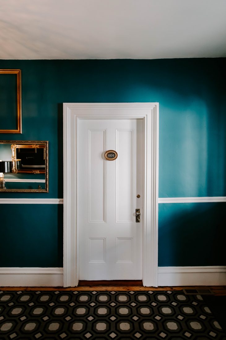 Teal wall gold picture frames white hotel room door