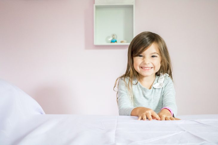 Little Girl standing bedside with purple sheets
