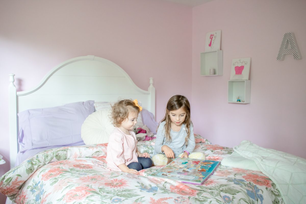Little girls playing on top of a queen size bed with a floral comforter