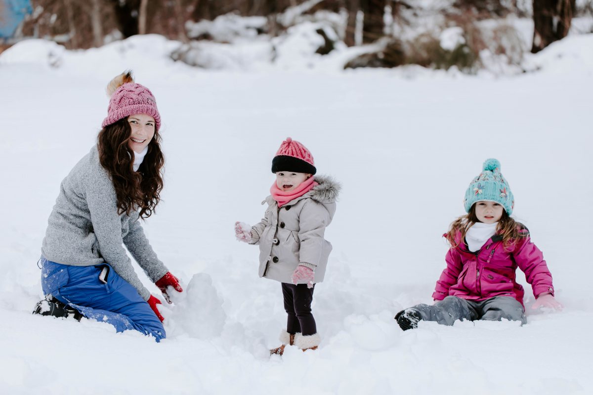 Woman wearing pink hat and winter clothes in the snow with little daughters wearing winter clothes in the snow 