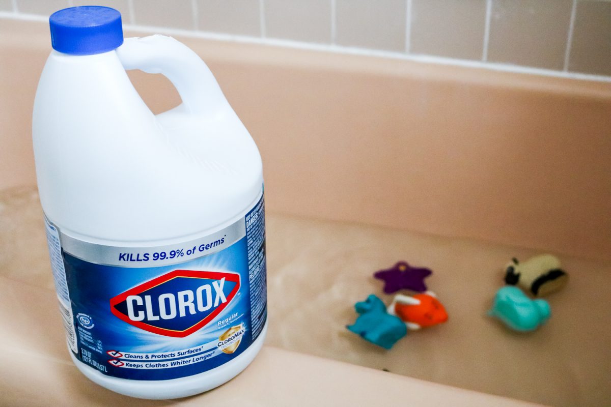 Toys soaking in water and bleach in a pink tiled bathtub and Clorox bottle on the edge of the bathtub