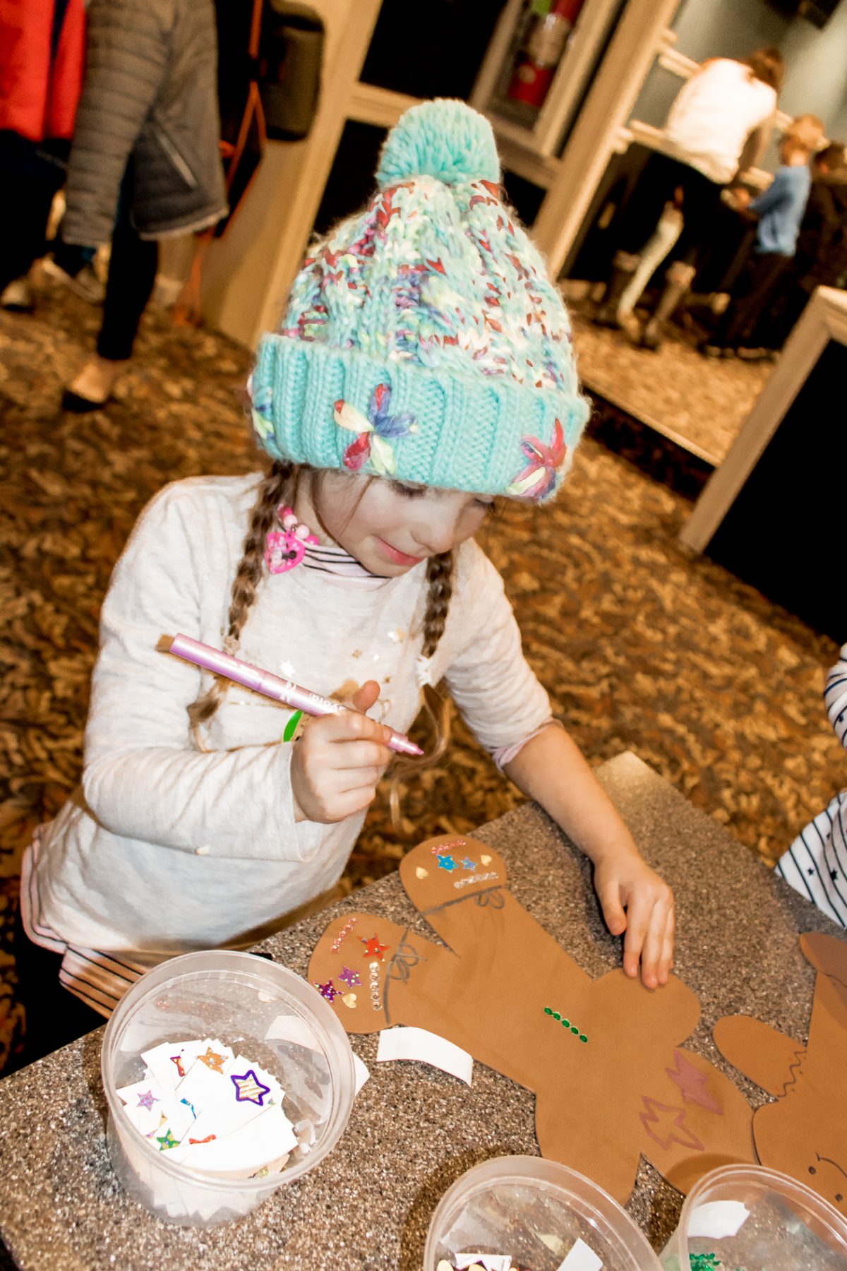 Little girl wearing tan sweater and blue winter hat smiling while making a gingerbread art projects at Woodloch Pines Resort Winter Festival