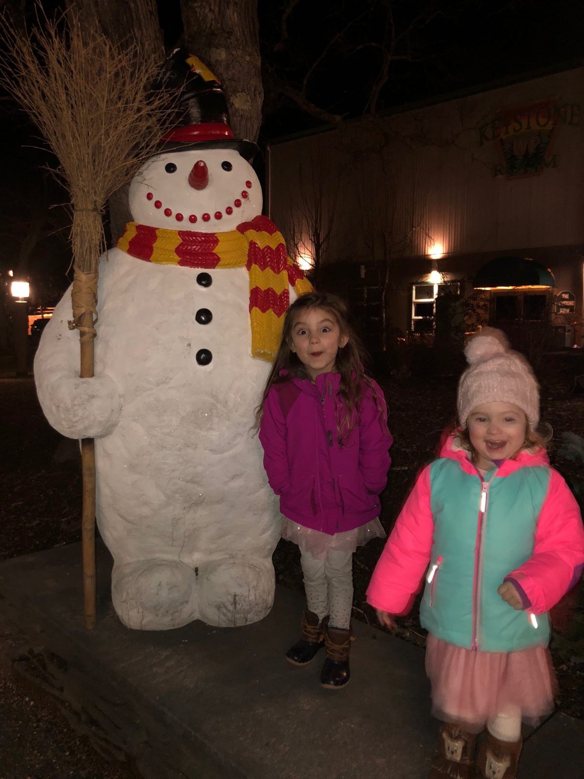 Little girls in winter coats standing by Frosty the Snowman statue at Woodloch Pines Resort in Poconos Mountains PA
