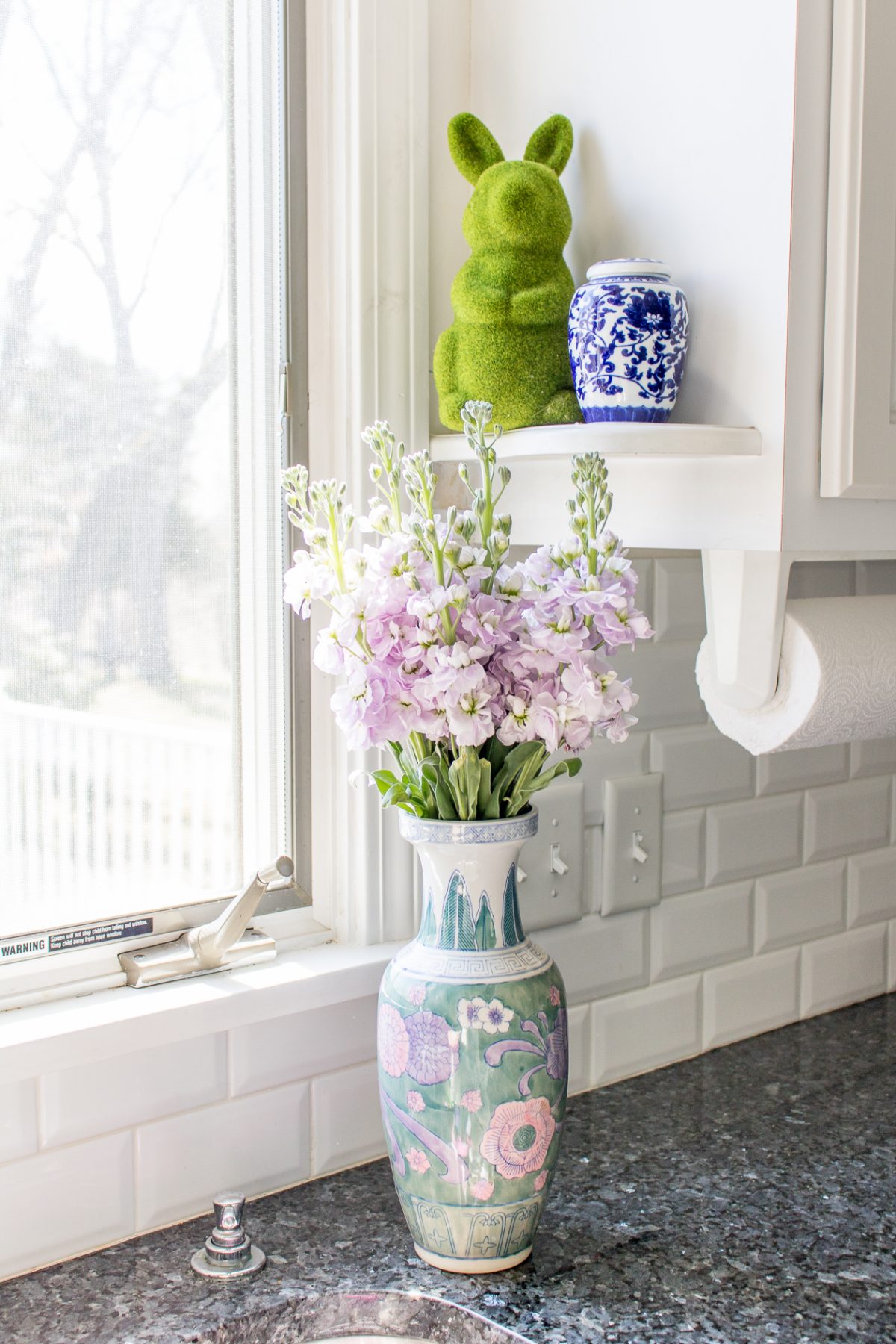 Green Moss Bunny, Blue Ginger Jar, Pastel Vase with Purple Flowers on Kitchen Counter