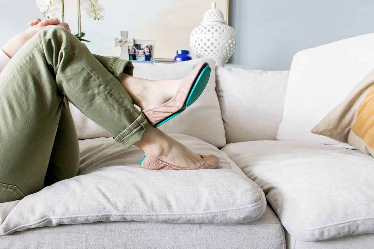 Woman's legs crossed wearing green pants and pink Tieks ballet flats with teal bottoms 