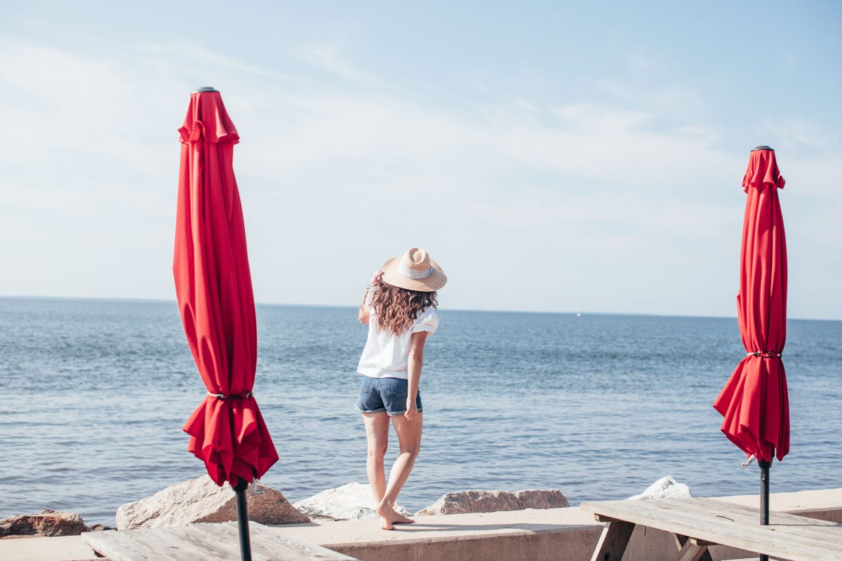 Woman wearing beach hat standing between two red umbrellas on beach wall