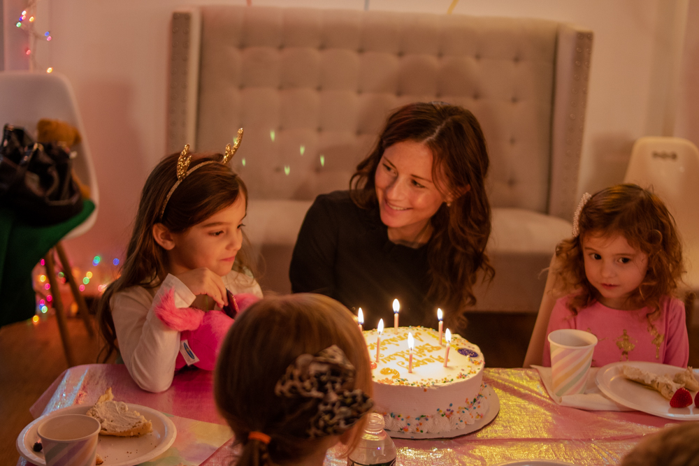 mom smiling at daughter sitting in front of birthday cake with lit candles