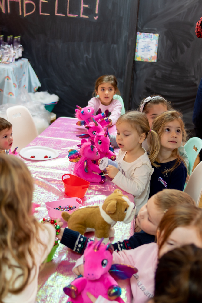 little girls sitting at craft table with stuffed unicorns