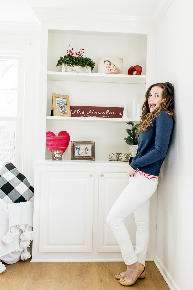 Woman wearing Blue Dudley Stephens Fleece with Red Stripe Shirt and White Denim in front of White Shelves with Valentine's Day Decor