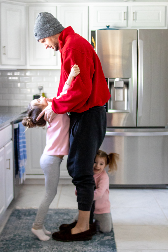 Dad in kitchen with kids hanging off of him