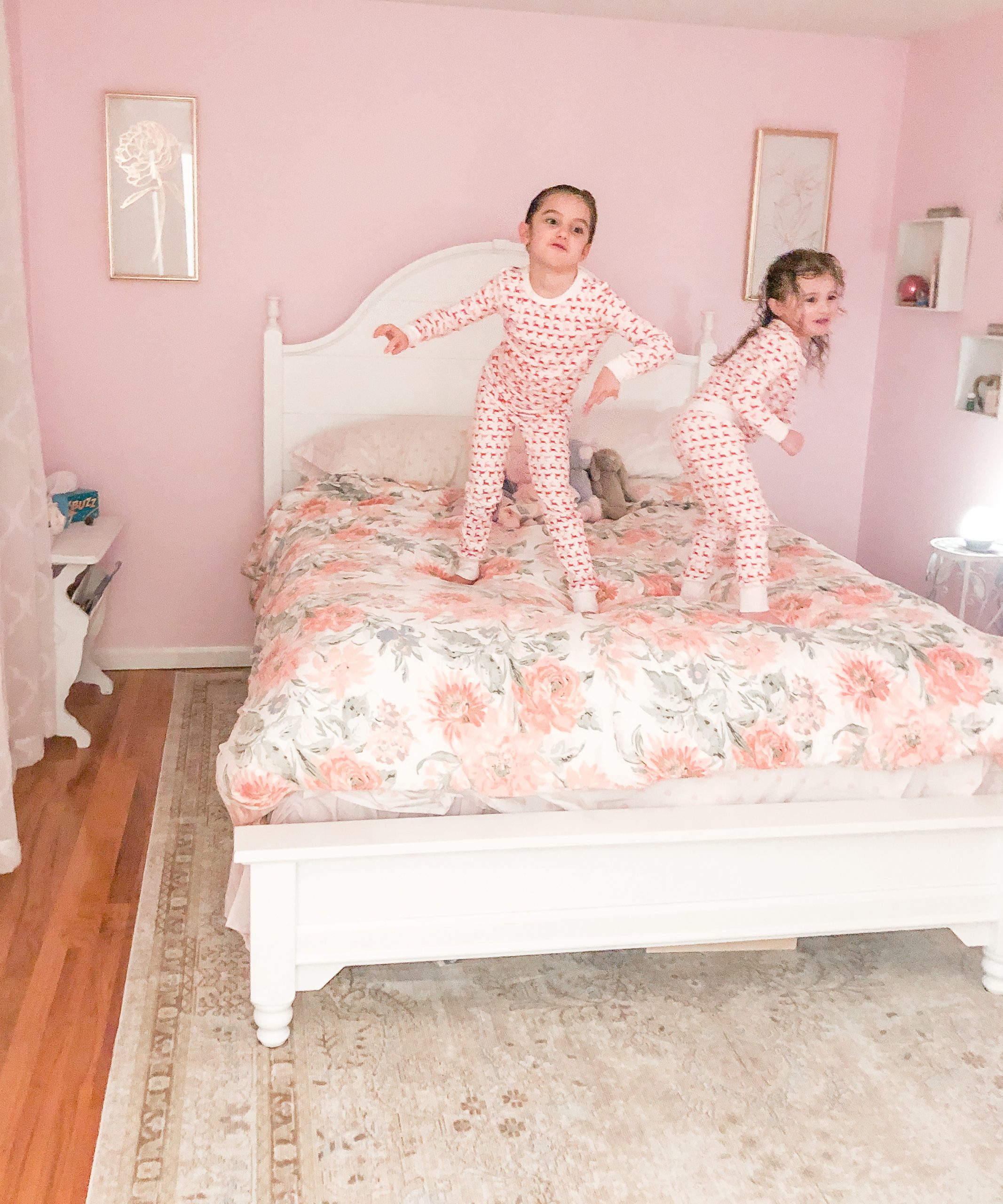 little girls jumping on bed in pink bedroom walls, white bed with floral bedding, white sheer curtains