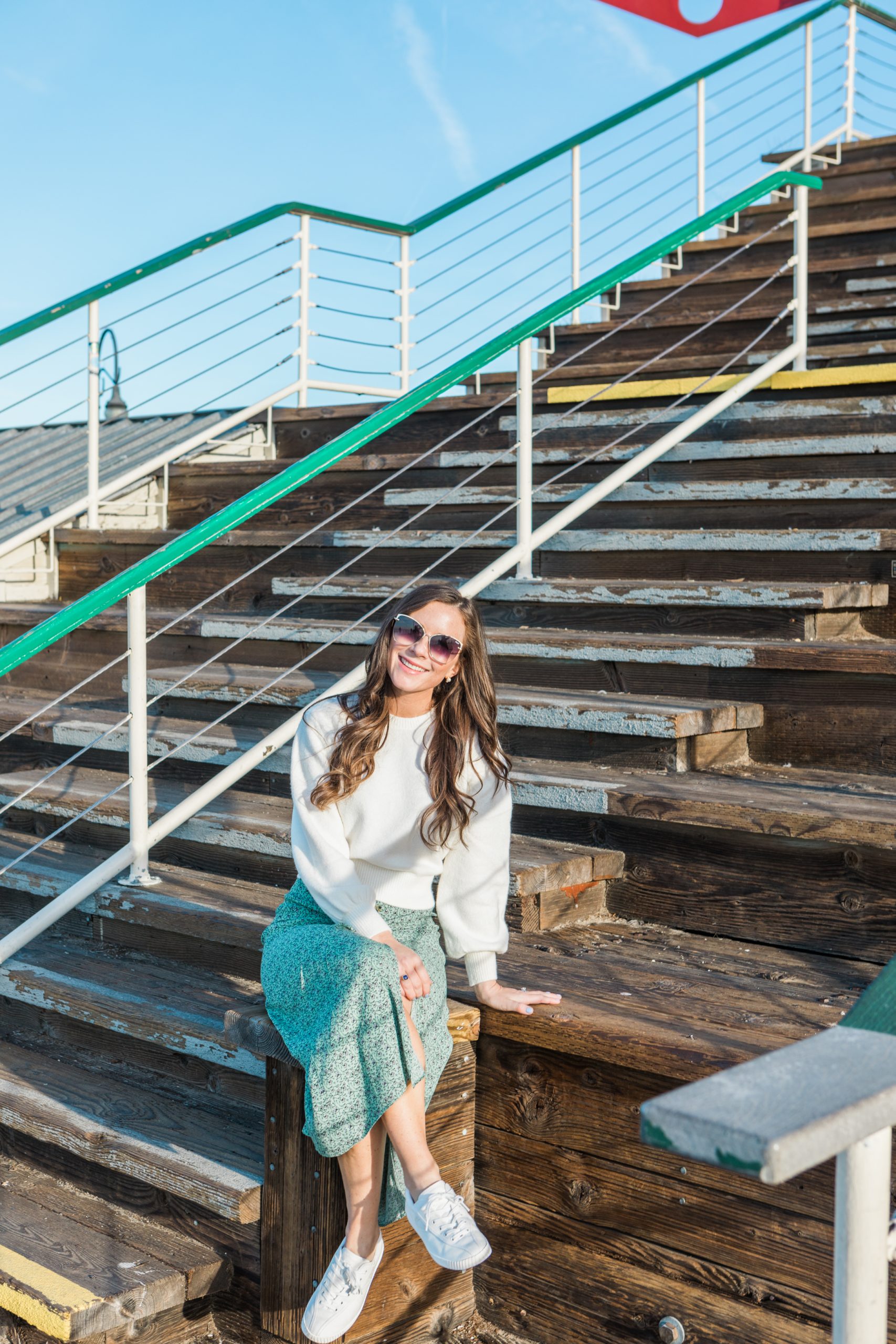 woman sitting on stairs in santa monica wearing a white shirt and green skirt with tretorn sneakers