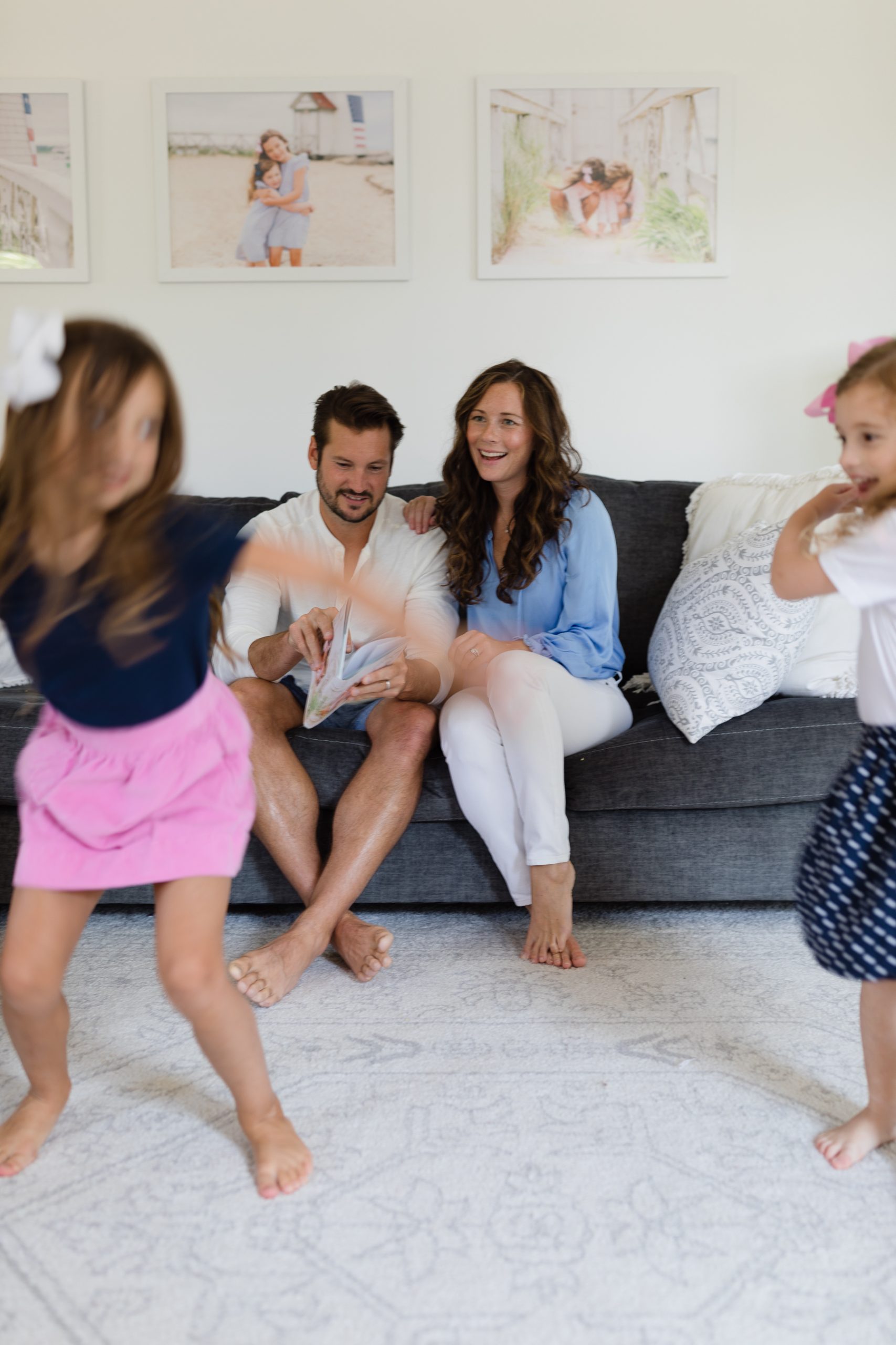 Mom and Dad on couch looking at photo book while girls dance in front of them