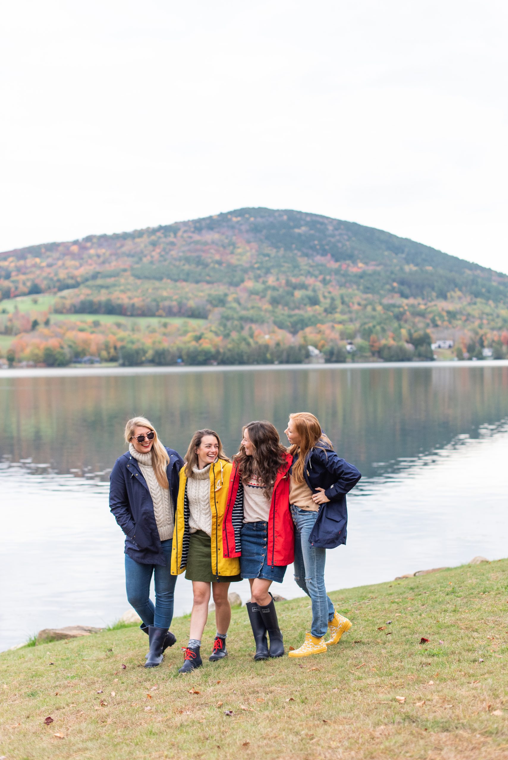 girlfriends wearing rain coats and rain boots from Joules standing in front of Vermont lake during the fall