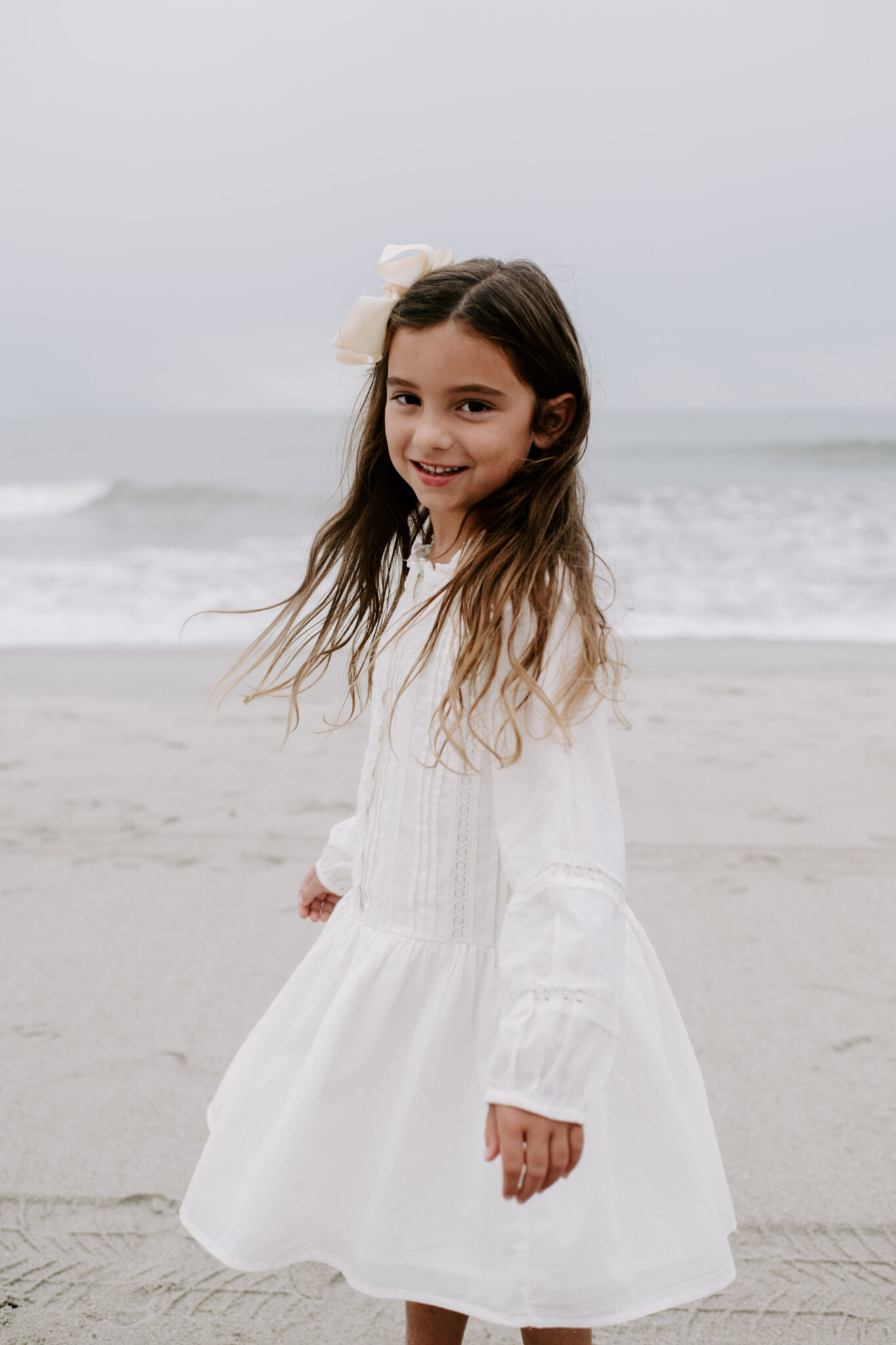 little girl in white dress twirling on beach