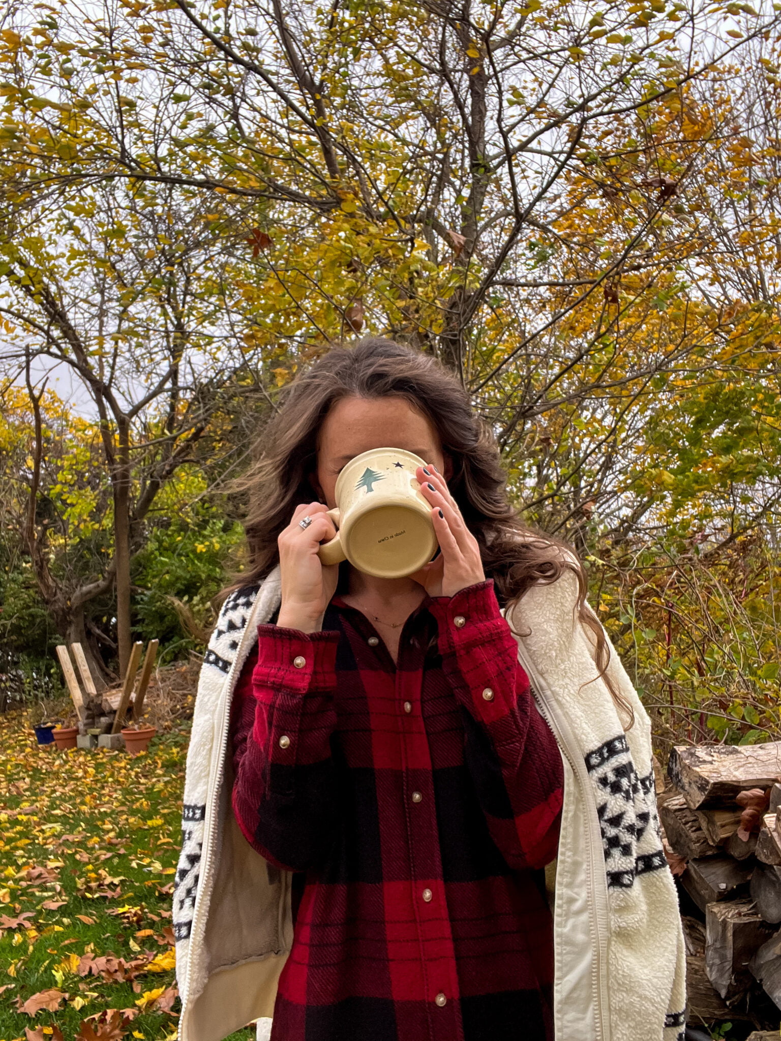 Caitlin houston sipping coffee wearing plaid flannel dress with fleece jacket over shoulders