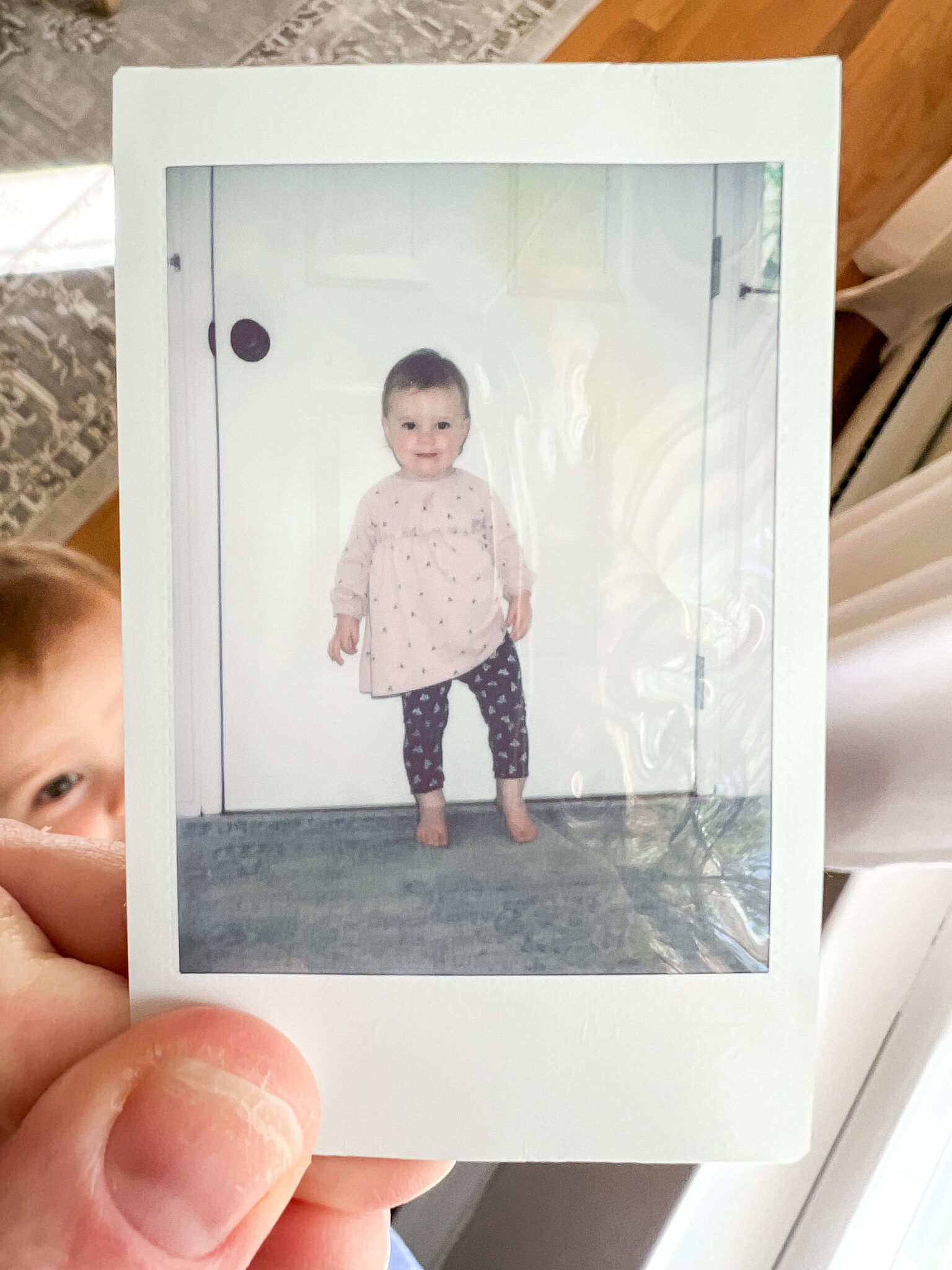 polaroid picture of toddler with toddler in background trying to grab the photo