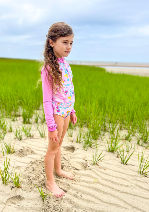 7 year old girl pink bathing suit standing on beach sea grass behind her