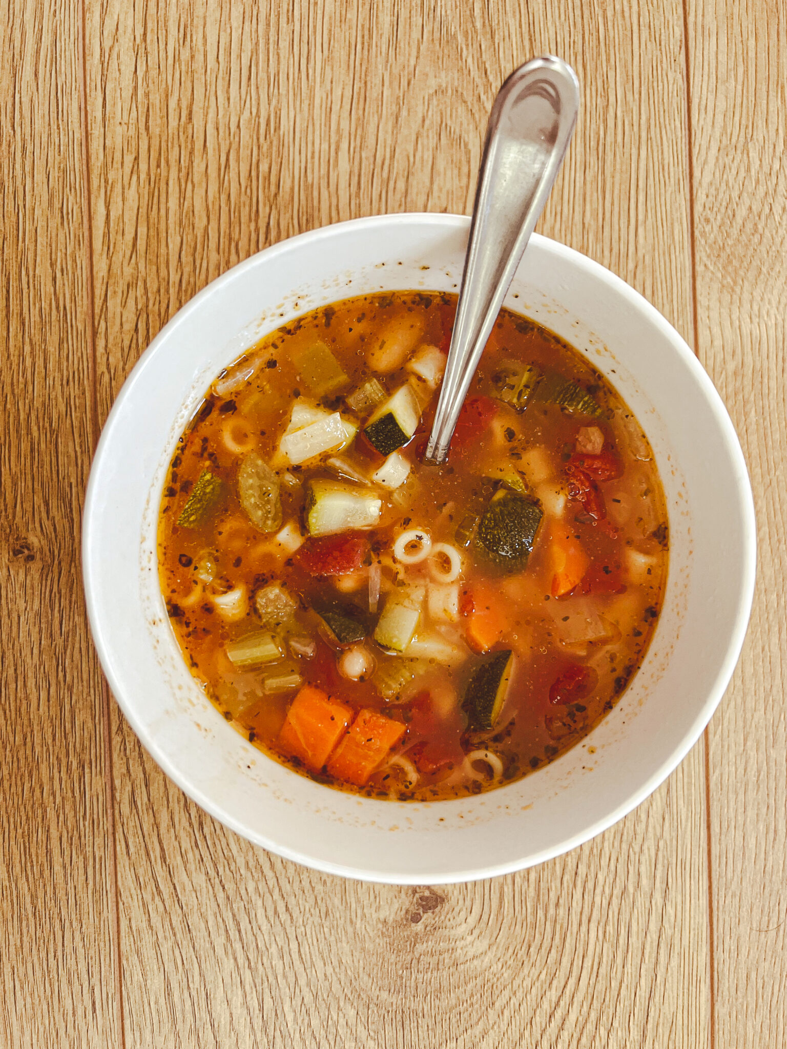 white bowl with spoon chunky minestrone soup zucchini ditalini tomato carrot