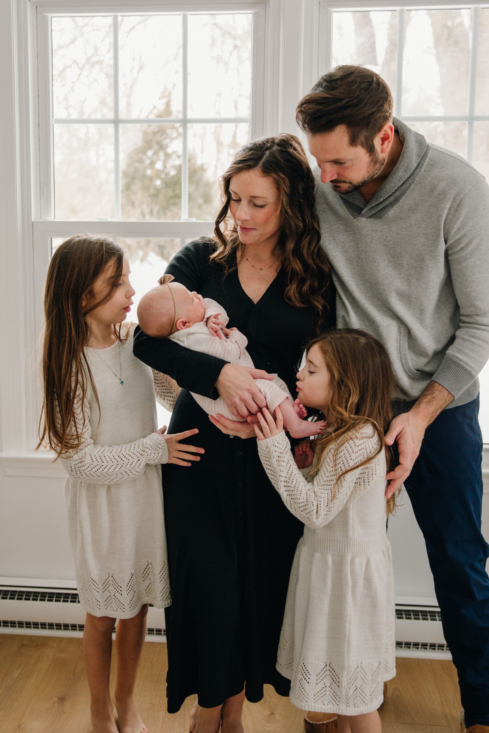 family of five mom holding newborn dad and big sisters looking at baby