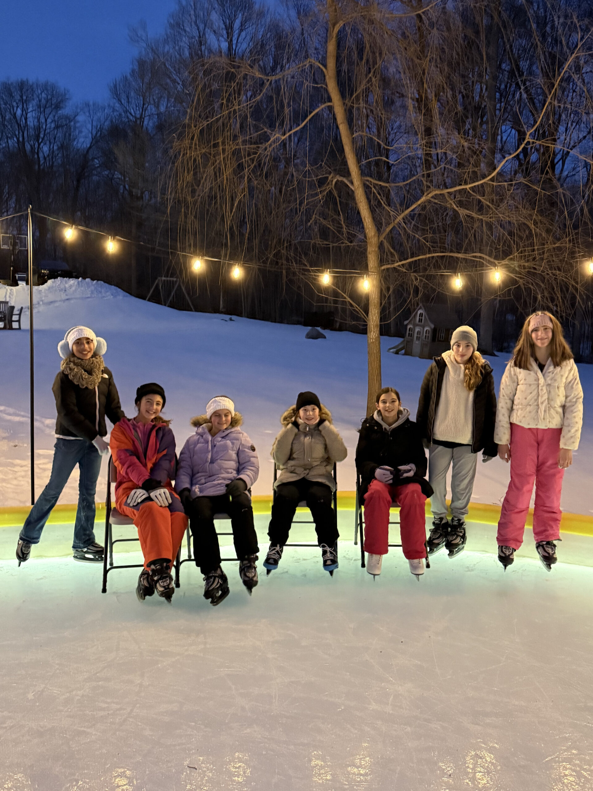 Girl friends on ice skates on backyard skating rink