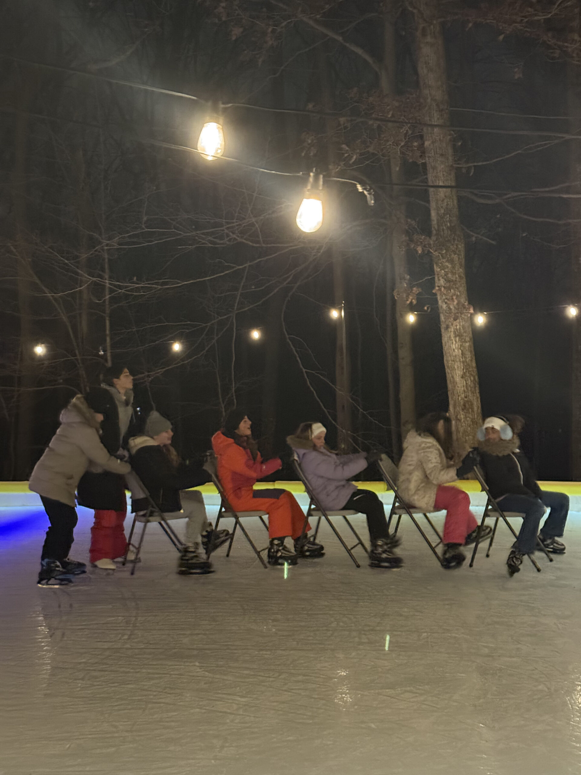 girls pushing each other on chairs on ice skating rink