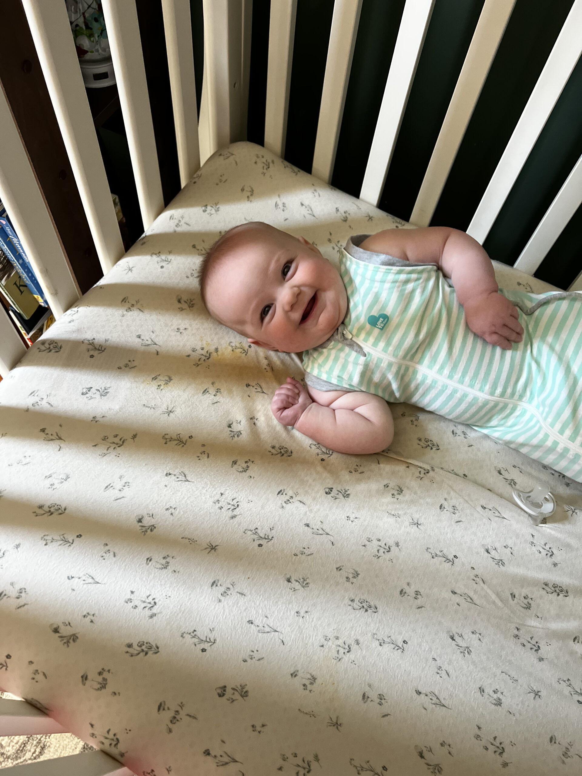 baby in sleep sack smiling in crib third child