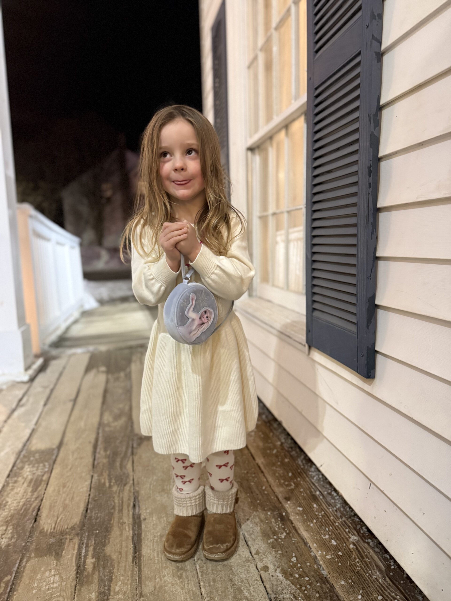 toddler wearing a purse and snow boots and holding hands together to say please