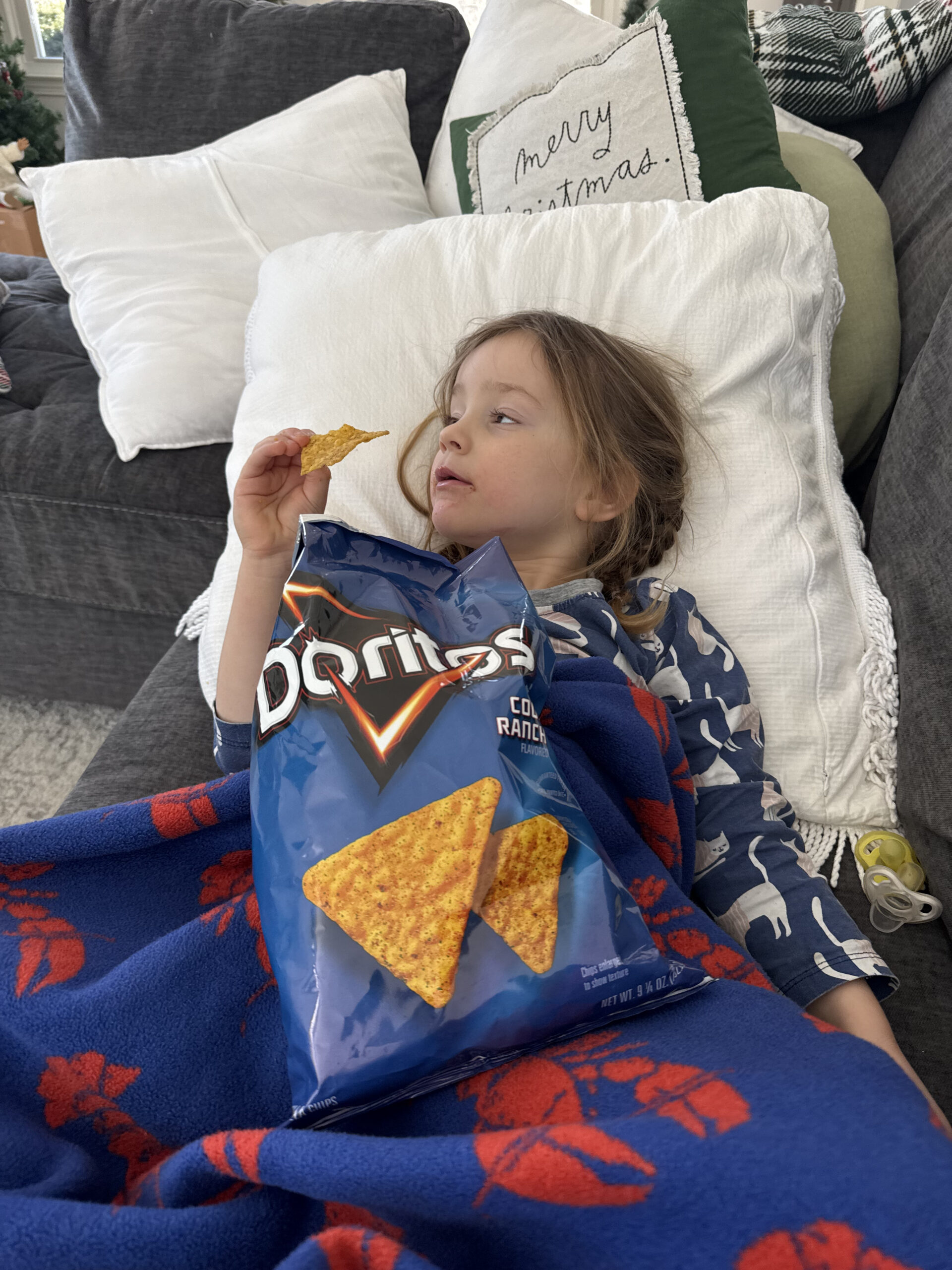 toddler with bag of doritos lying on couch