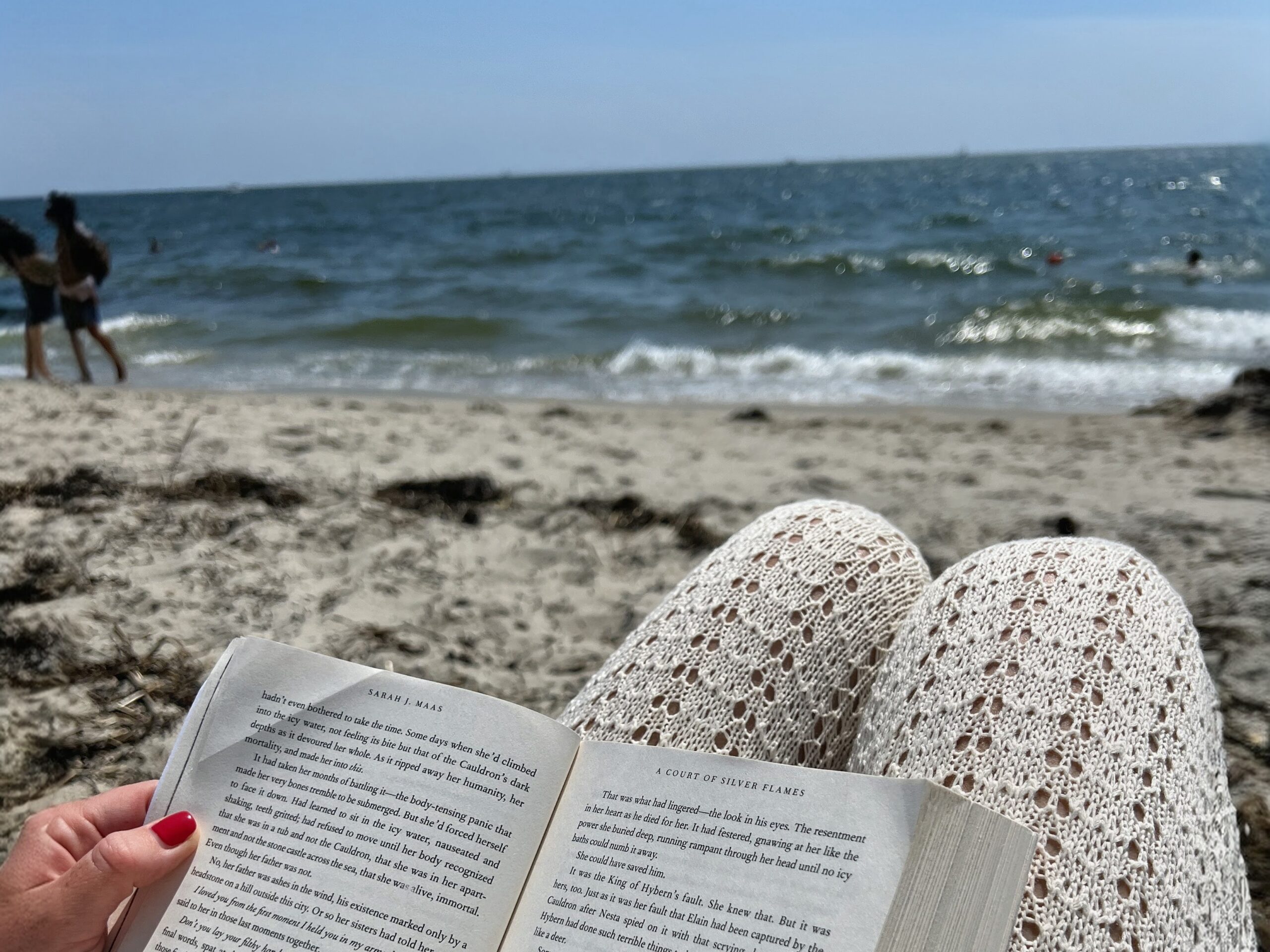book open on womans legs in front of ocean reading at the beach