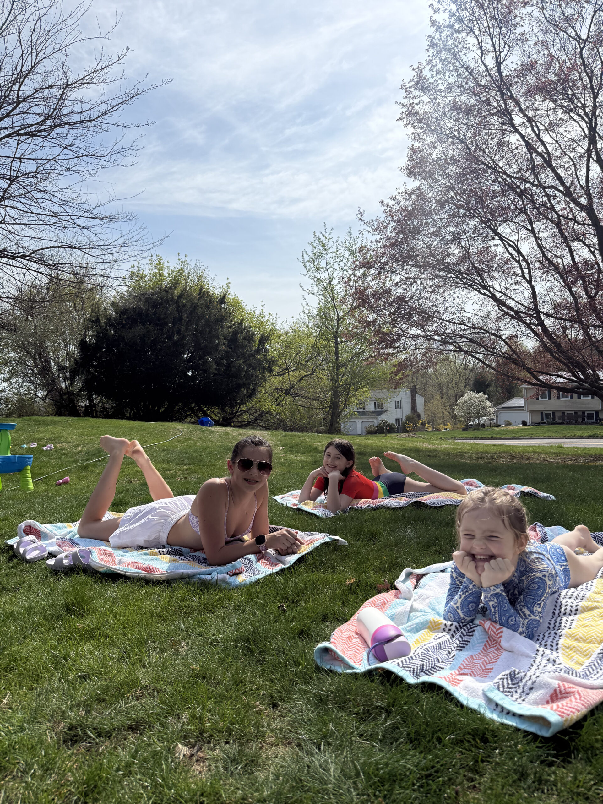 tween and toddler laying on towels in the yard with sprinkler in the background summer screen free activities