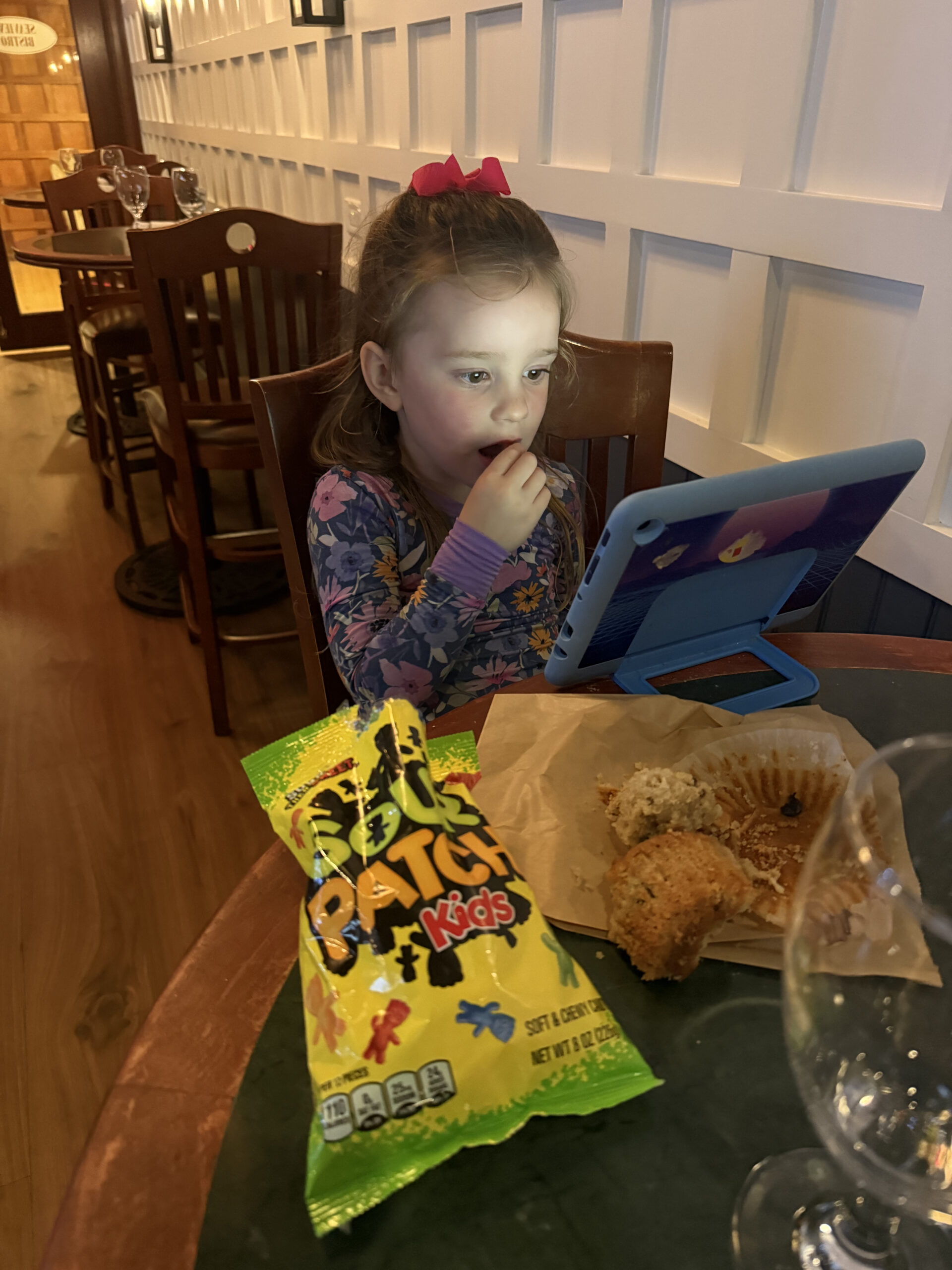 toddler at bar top table wearing pajamas eating candy and a muffin watching ipad